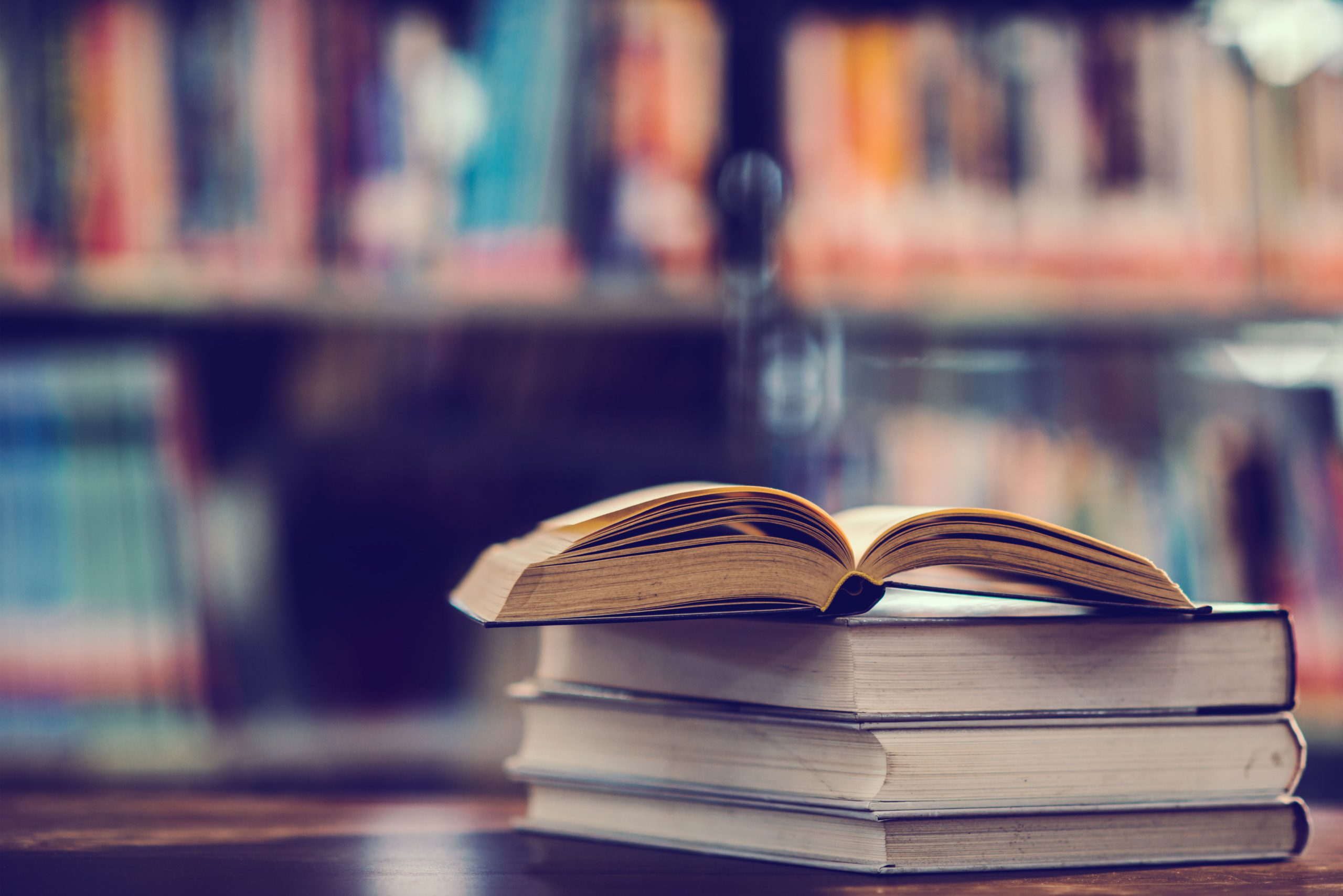 A stack of books on a table in front of a library, showcasing college facilities and resources for students.