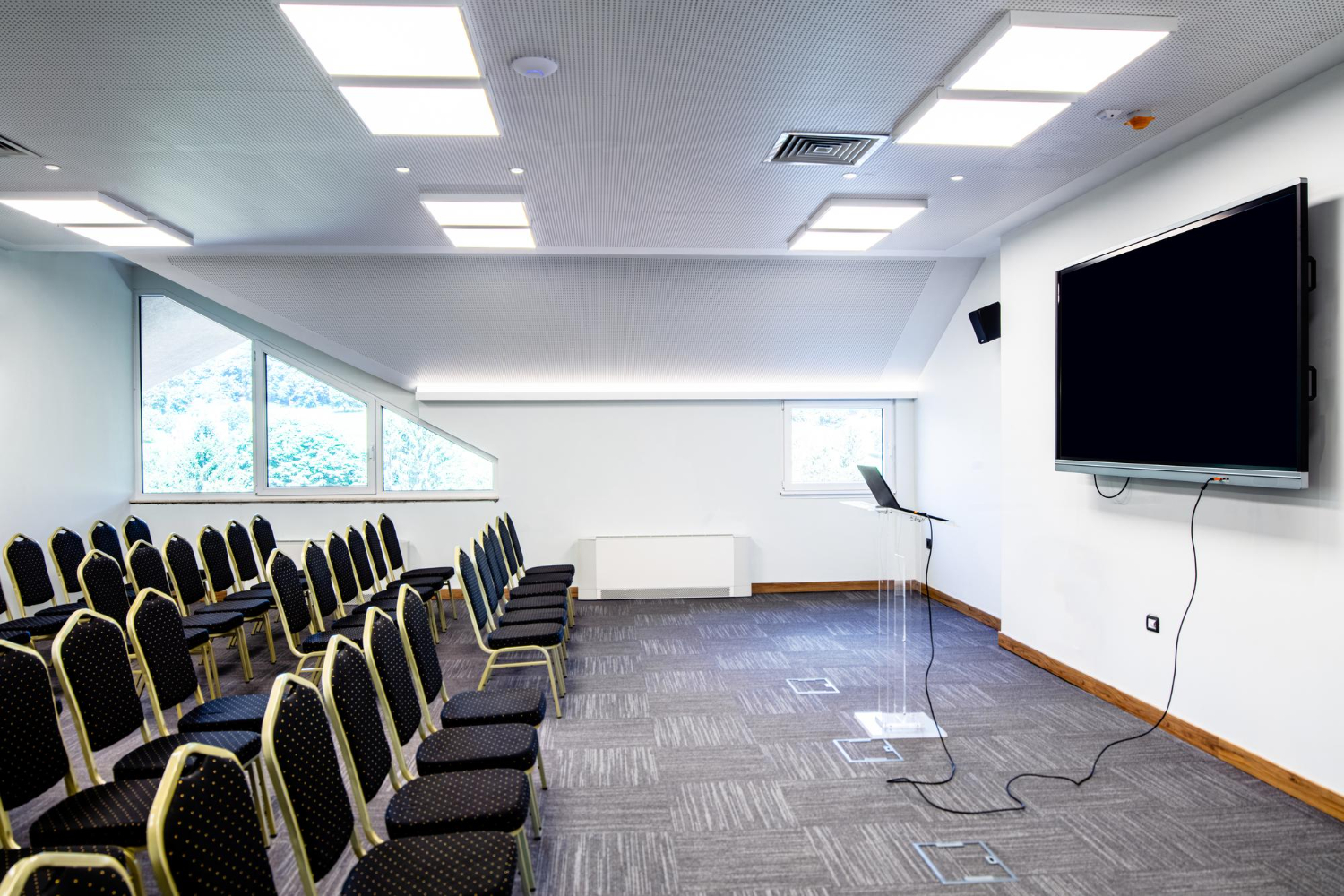 Interior of CAT Degree College seminar hall with black chairs arranged around a large flat screen TV.